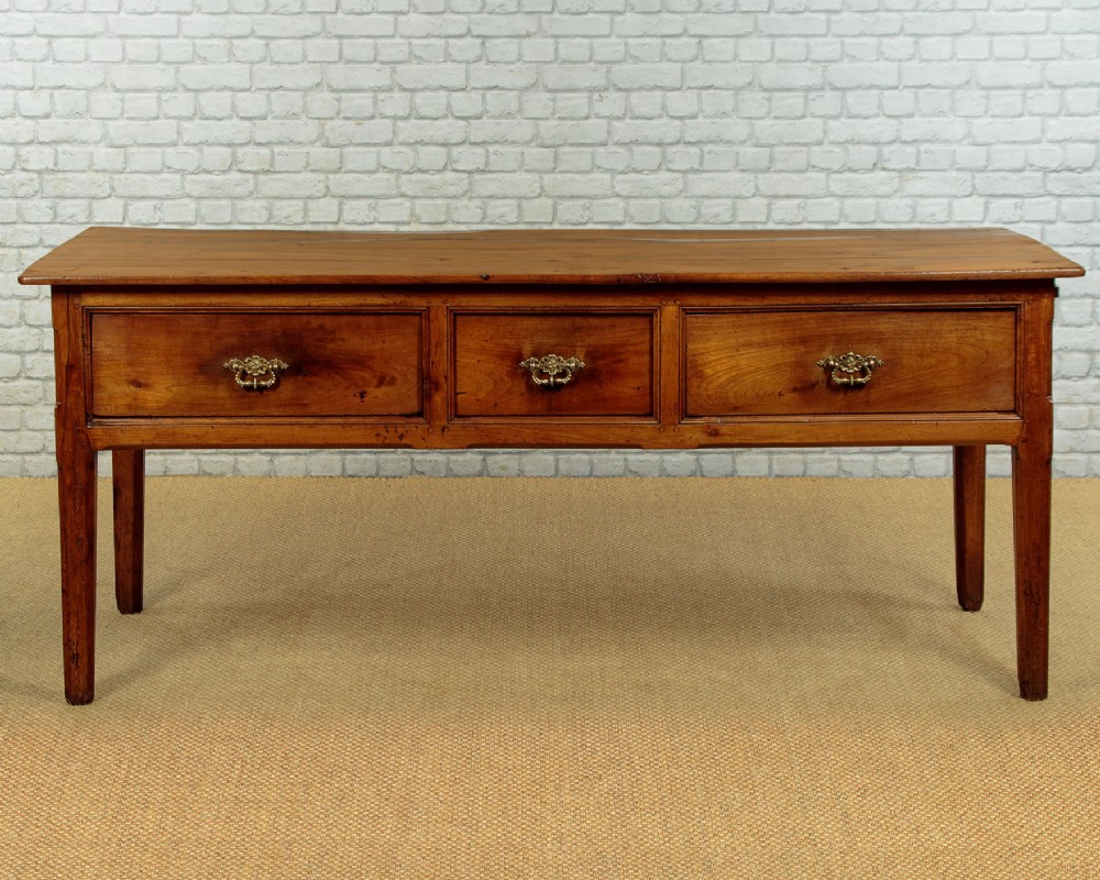 A mid-19th-century French cherry wood kitchen work table featuring three front drawers with brass handles and tapered square legs.