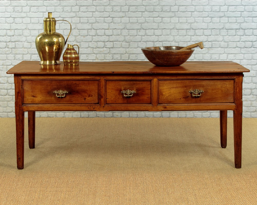 A mid-19th-century French cherry wood kitchen work table featuring three front drawers with brass handles and tapered square legs. View II