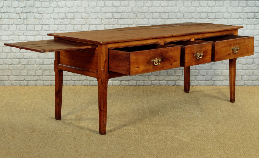 A mid-19th-century French cherry wood kitchen work table featuring three front drawers with brass handles and tapered square legs. View IV