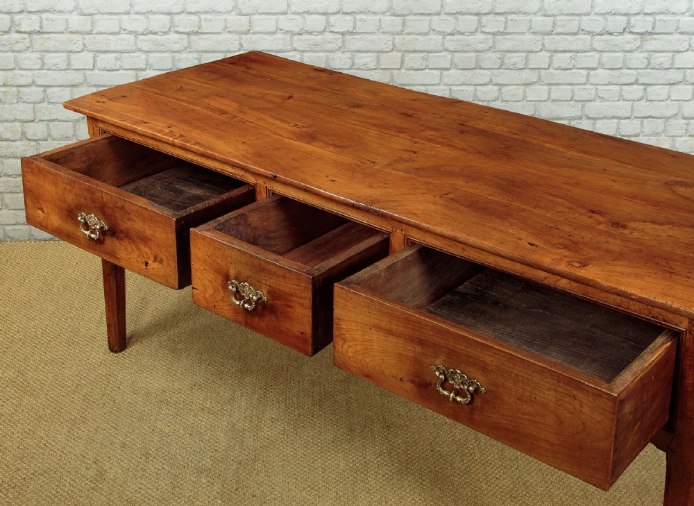 A mid-19th-century French cherry wood kitchen work table featuring three front drawers with brass handles and tapered square legs. View XII