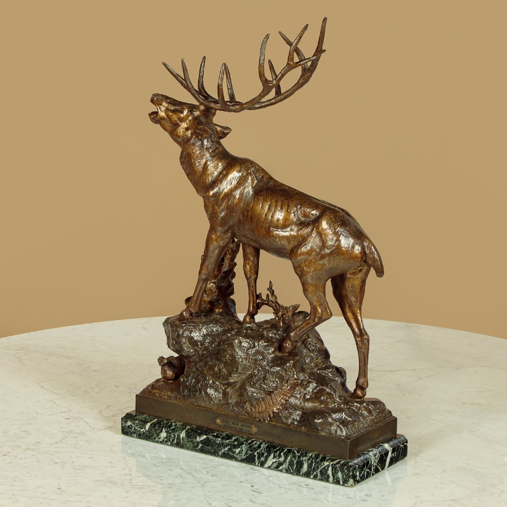 A bronze-patinated spelter sculpture depicting a bellowing stag on a rocky outcrop, mounted on a veined green marble base with a metallic title plaque. View III