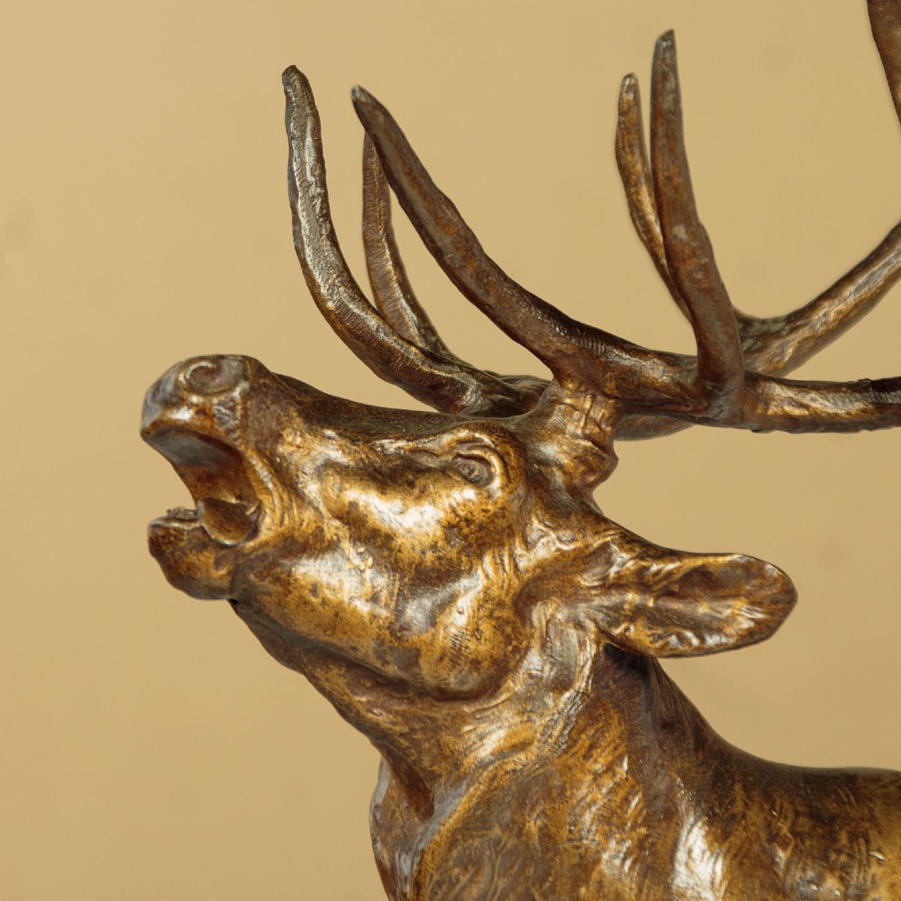 A bronze-patinated spelter sculpture depicting a bellowing stag on a rocky outcrop, mounted on a veined green marble base with a metallic title plaque. View V