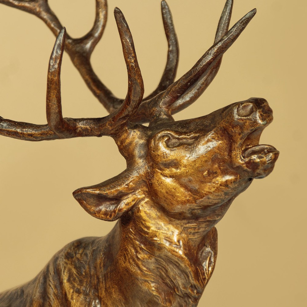 A bronze-patinated spelter sculpture depicting a bellowing stag on a rocky outcrop, mounted on a veined green marble base with a metallic title plaque. View VI