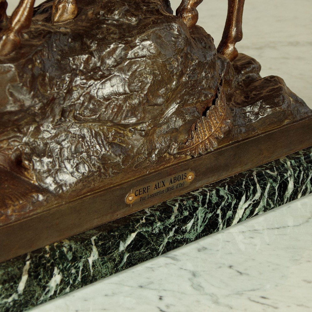 A bronze-patinated spelter sculpture depicting a bellowing stag on a rocky outcrop, mounted on a veined green marble base with a metallic title plaque. View IX