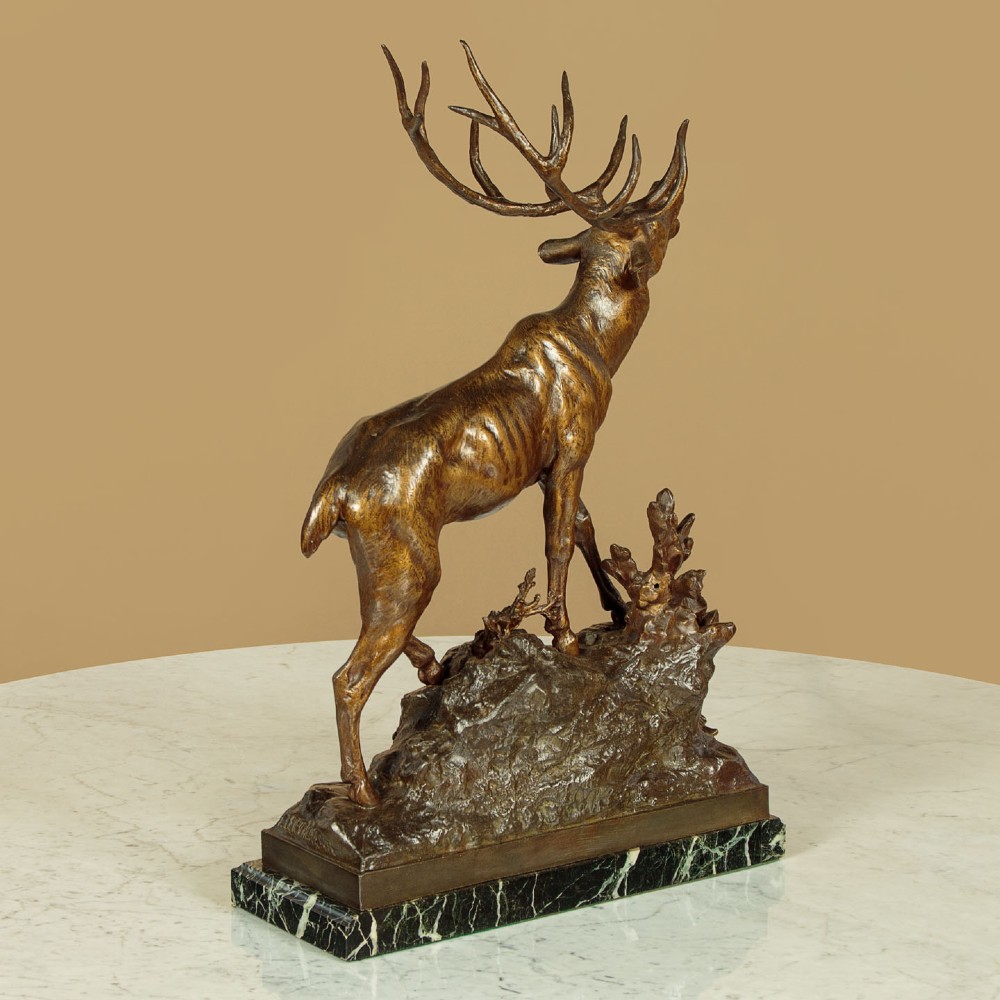 A bronze-patinated spelter sculpture depicting a bellowing stag on a rocky outcrop, mounted on a veined green marble base with a metallic title plaque. View XI