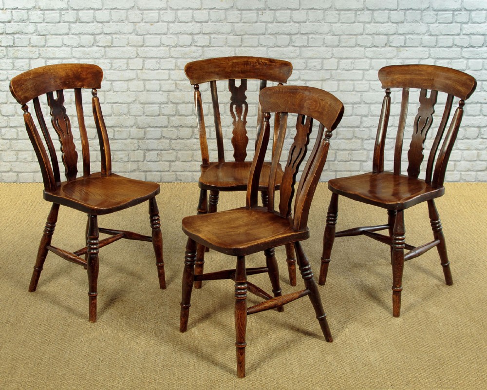 A set of four late 19th-century dark oak dining chairs featuring shaped back rails, pierced splats, contoured wooden seats, and turned legs with stretchers.