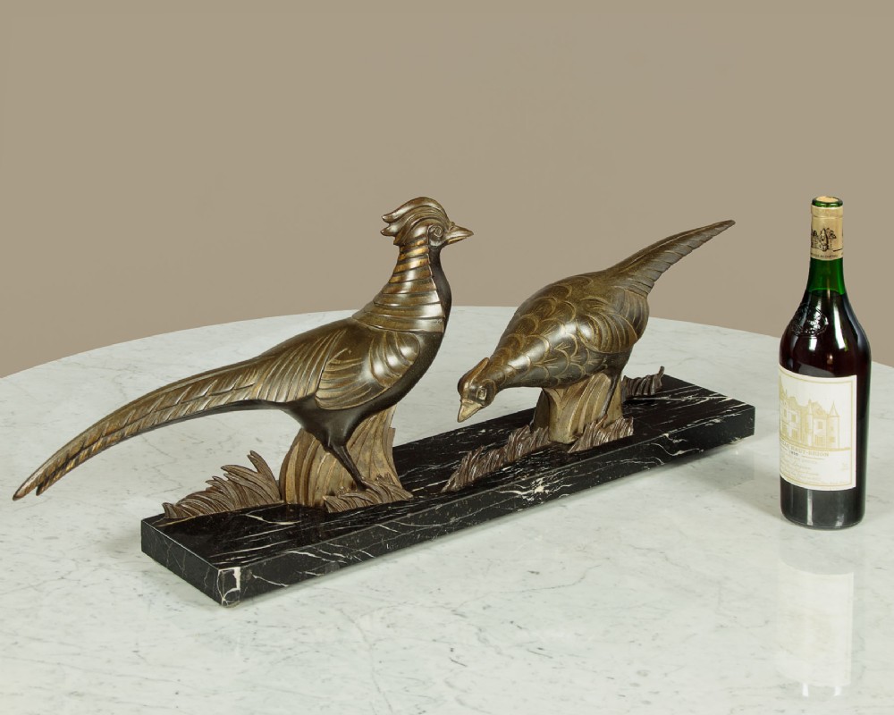 An Art Deco patinated metal sculpture featuring two stylised pheasants mounted on a rectangular black marble base with white veining. View II