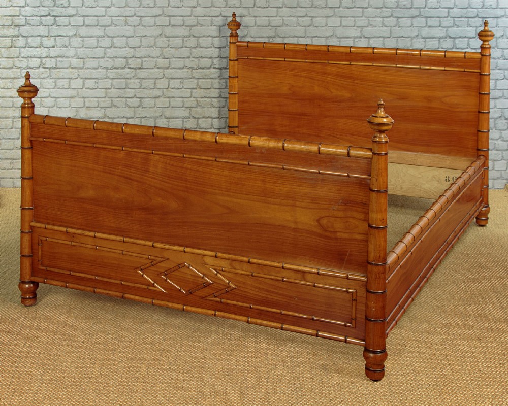 A late 19th-century faux bamboo double bed frame in warm brown wood, featuring turned bamboo-effect posts, finials, and panelled headboard and footboard.