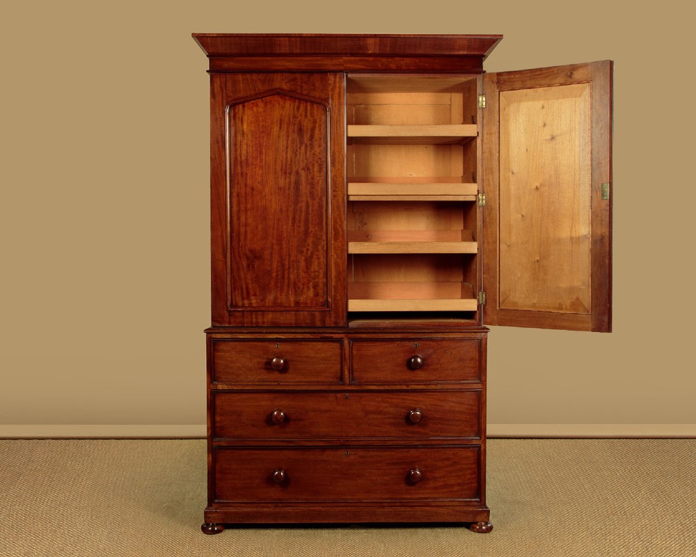 A nineteenth-century mahogany linen press featuring flame mahogany panel doors opening to reveal timber trays above a base of four drawers with turned wooden knobs.