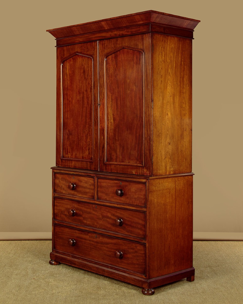 A nineteenth-century mahogany linen press featuring flame mahogany panel doors opening to reveal timber trays above a base of four drawers with turned wooden knobs. View IV