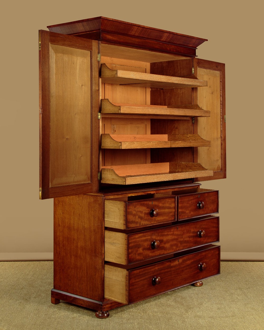 A nineteenth-century mahogany linen press featuring flame mahogany panel doors opening to reveal timber trays above a base of four drawers with turned wooden knobs. View V