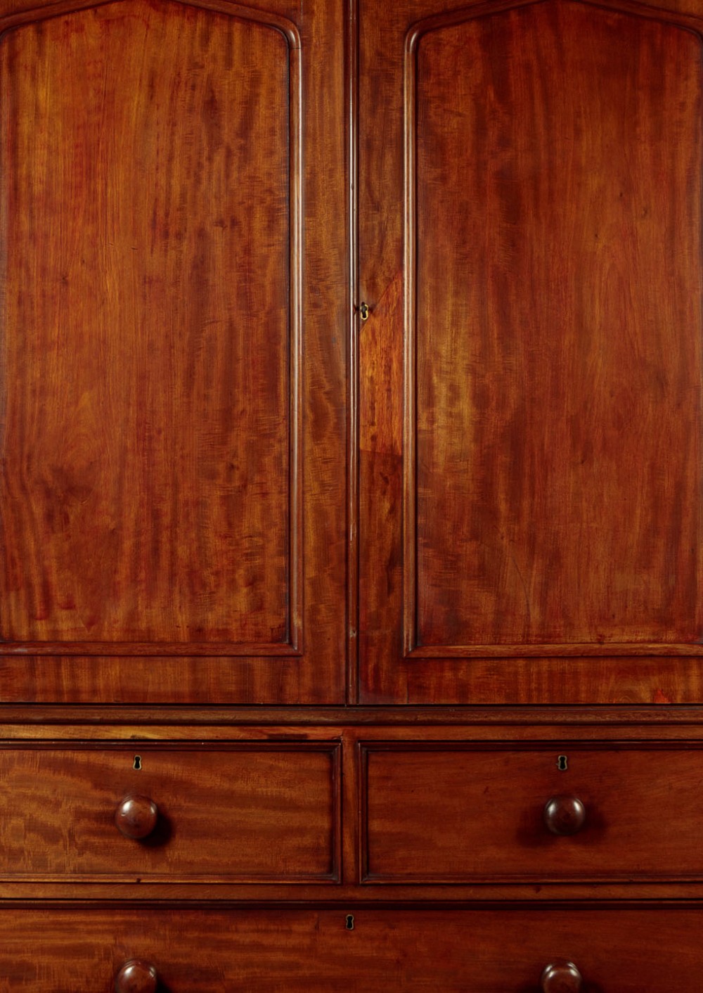 A nineteenth-century mahogany linen press featuring flame mahogany panel doors opening to reveal timber trays above a base of four drawers with turned wooden knobs. View VII