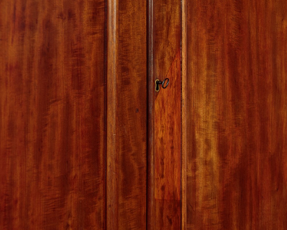 A nineteenth-century mahogany linen press featuring flame mahogany panel doors opening to reveal timber trays above a base of four drawers with turned wooden knobs. View VIII