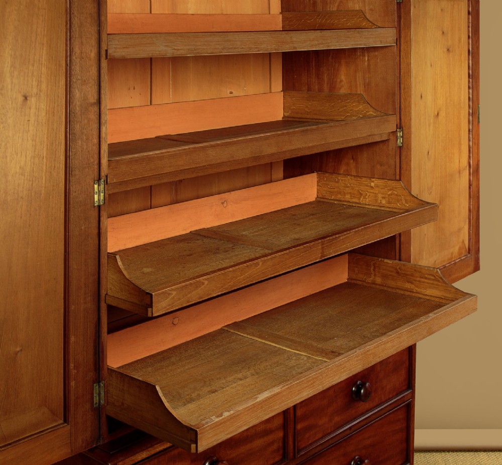 A nineteenth-century mahogany linen press featuring flame mahogany panel doors opening to reveal timber trays above a base of four drawers with turned wooden knobs. View IX