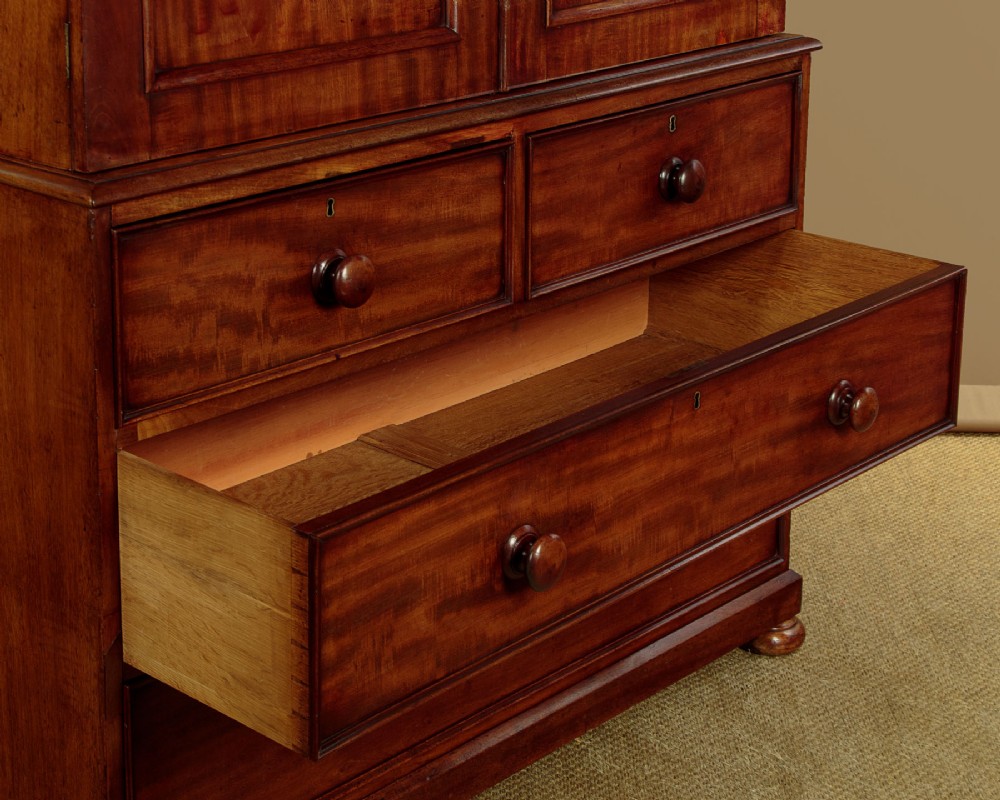 A nineteenth-century mahogany linen press featuring flame mahogany panel doors opening to reveal timber trays above a base of four drawers with turned wooden knobs. View X