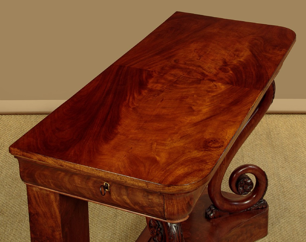 A 19th-century Victorian mahogany console table featuring carved S-scroll front supports and a concave plinth base. View VI