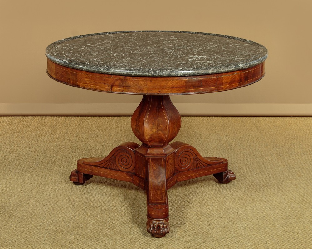 A 19th-century circular gueridon centre table featuring a dark grey marble top, warm walnut veneer with string inlay, a bulbous pedestal, and carved paw feet.