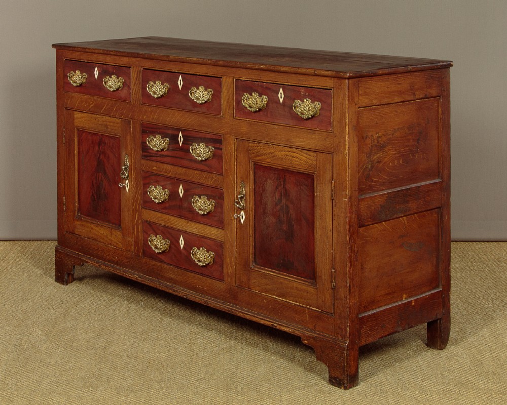 An antique 19th-century painted pine dresser base with central drawers, two side cupboard doors, red painted accent panels, and brass handles. View III