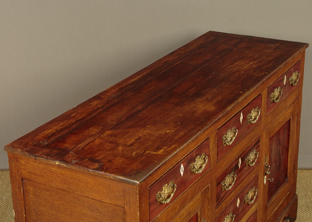 An antique 19th-century painted pine dresser base with central drawers, two side cupboard doors, red painted accent panels, and brass handles. View IV