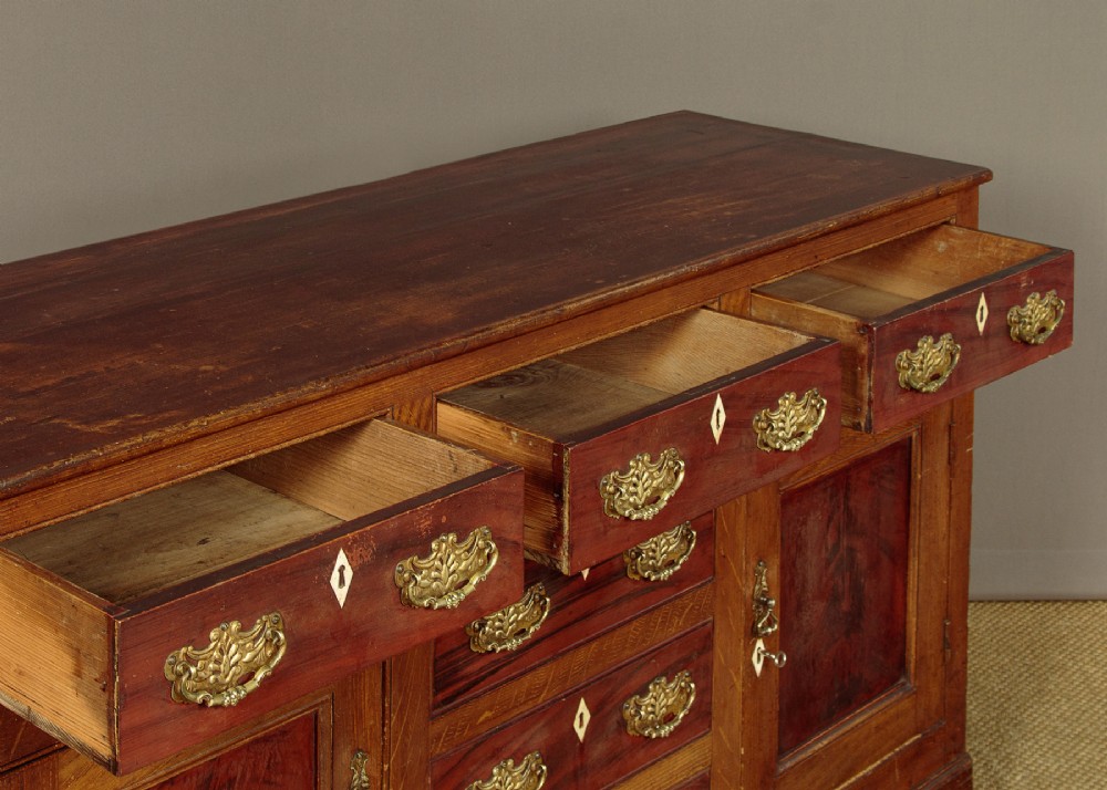 An antique 19th-century painted pine dresser base with central drawers, two side cupboard doors, red painted accent panels, and brass handles. View IX