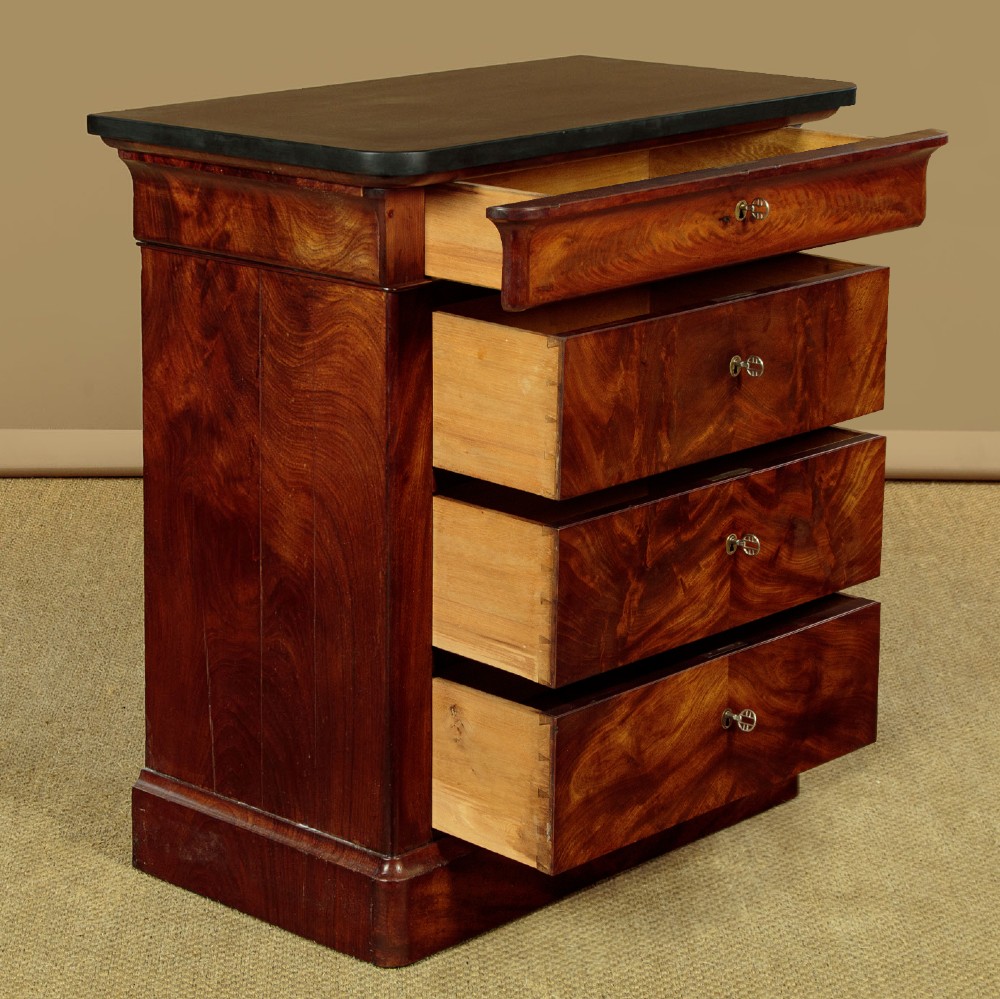 A nineteenth-century flame mahogany commode chest with four drawers, brass escutcheons, a dark slate top surface, and a plinth base. View IV