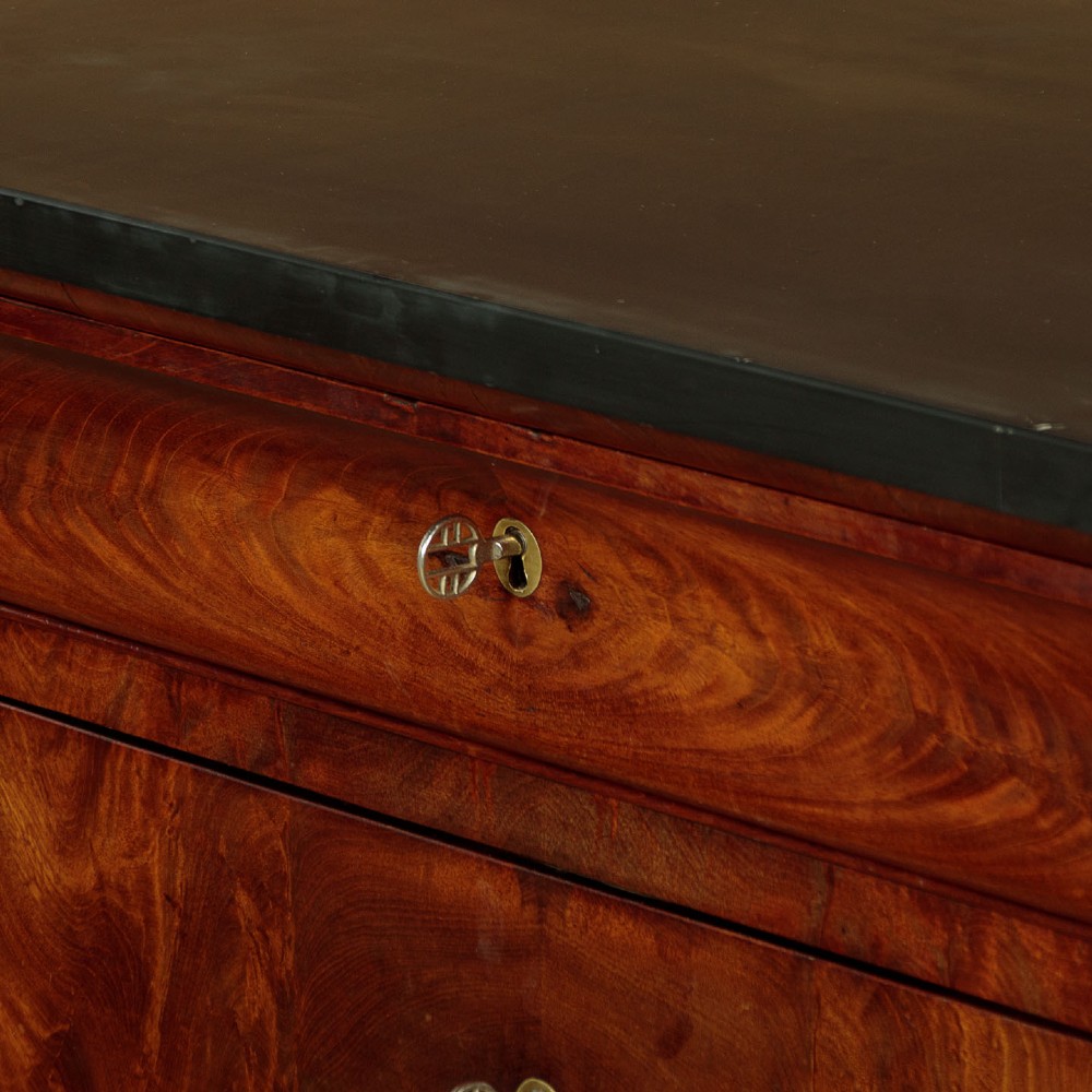 A nineteenth-century flame mahogany commode chest with four drawers, brass escutcheons, a dark slate top surface, and a plinth base. View VII