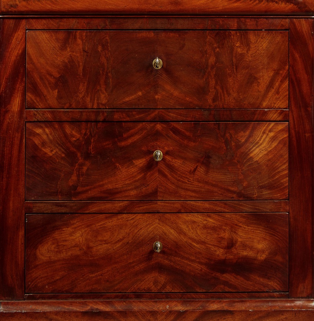 A nineteenth-century flame mahogany commode chest with four drawers, brass escutcheons, a dark slate top surface, and a plinth base. View VIII