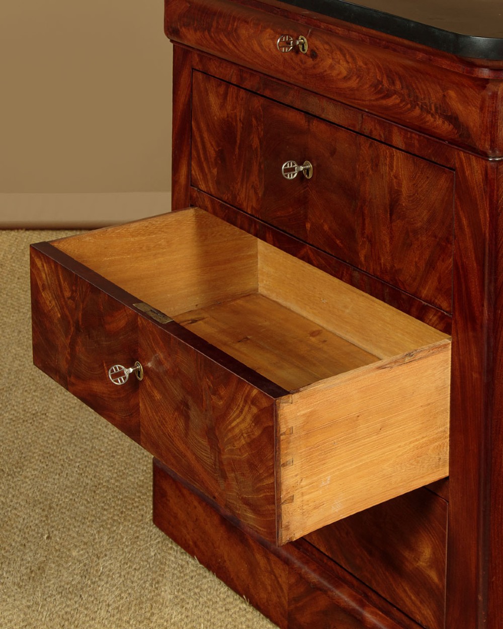 A nineteenth-century flame mahogany commode chest with four drawers, brass escutcheons, a dark slate top surface, and a plinth base. View XI