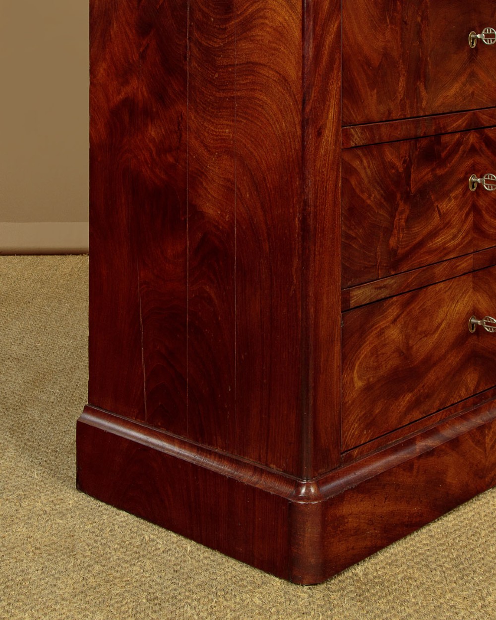 A nineteenth-century flame mahogany commode chest with four drawers, brass escutcheons, a dark slate top surface, and a plinth base. View XII