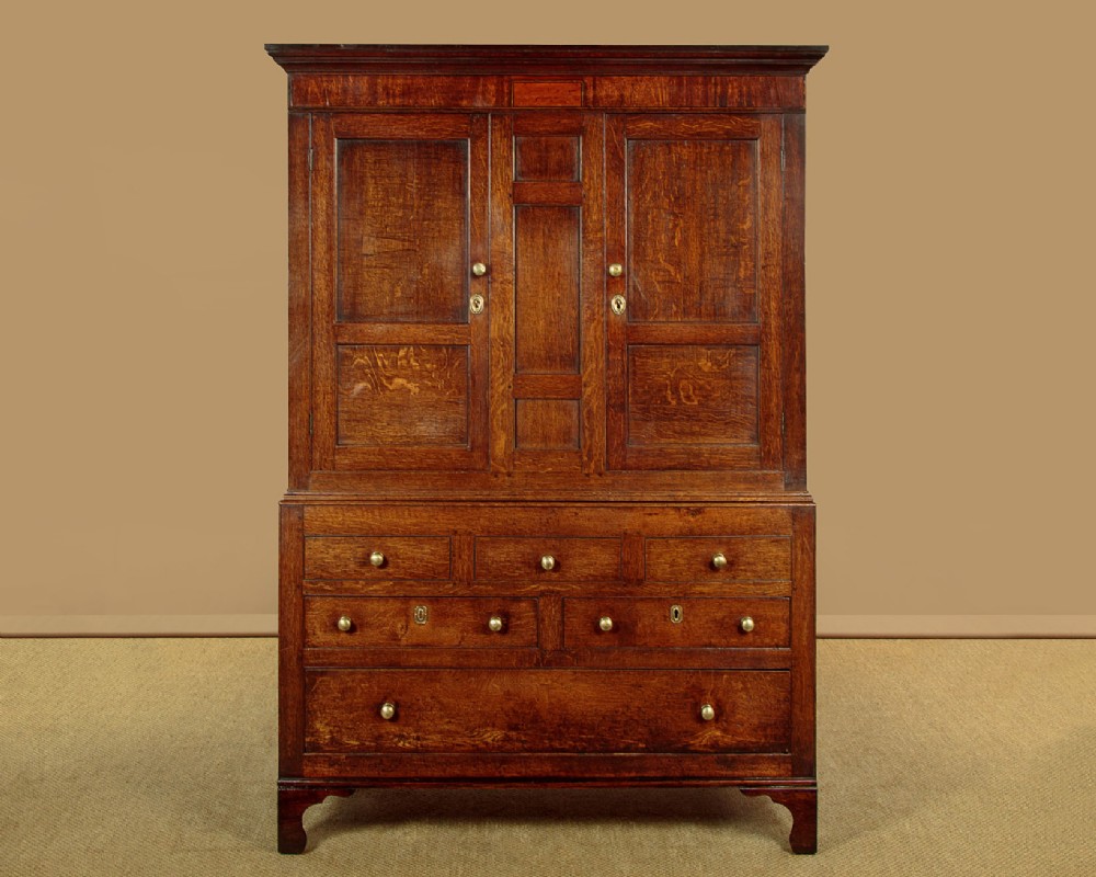 A nineteenth-century Welsh oak tack cupboard featuring a fielded twin-panel door upper section set over a chest of seven drawers with brass turned knobs.