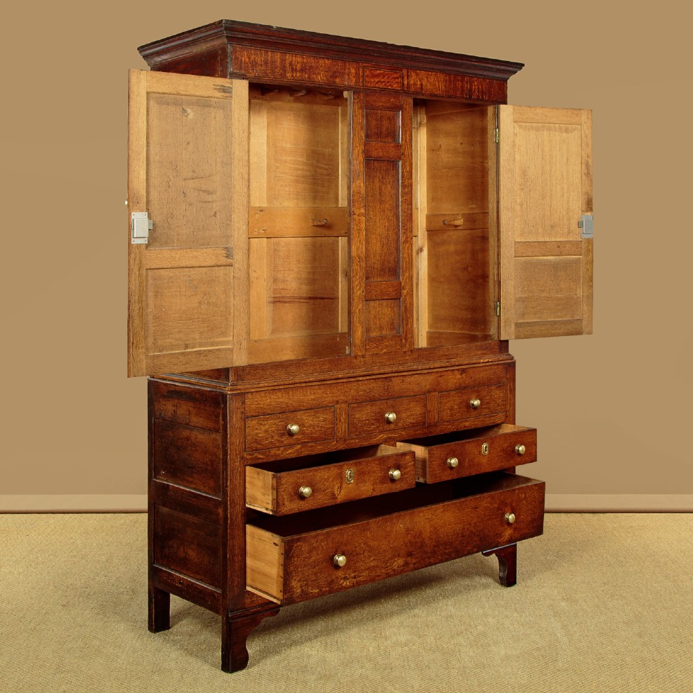 A nineteenth-century Welsh oak tack cupboard featuring a fielded twin-panel door upper section set over a chest of seven drawers with brass turned knobs. View V