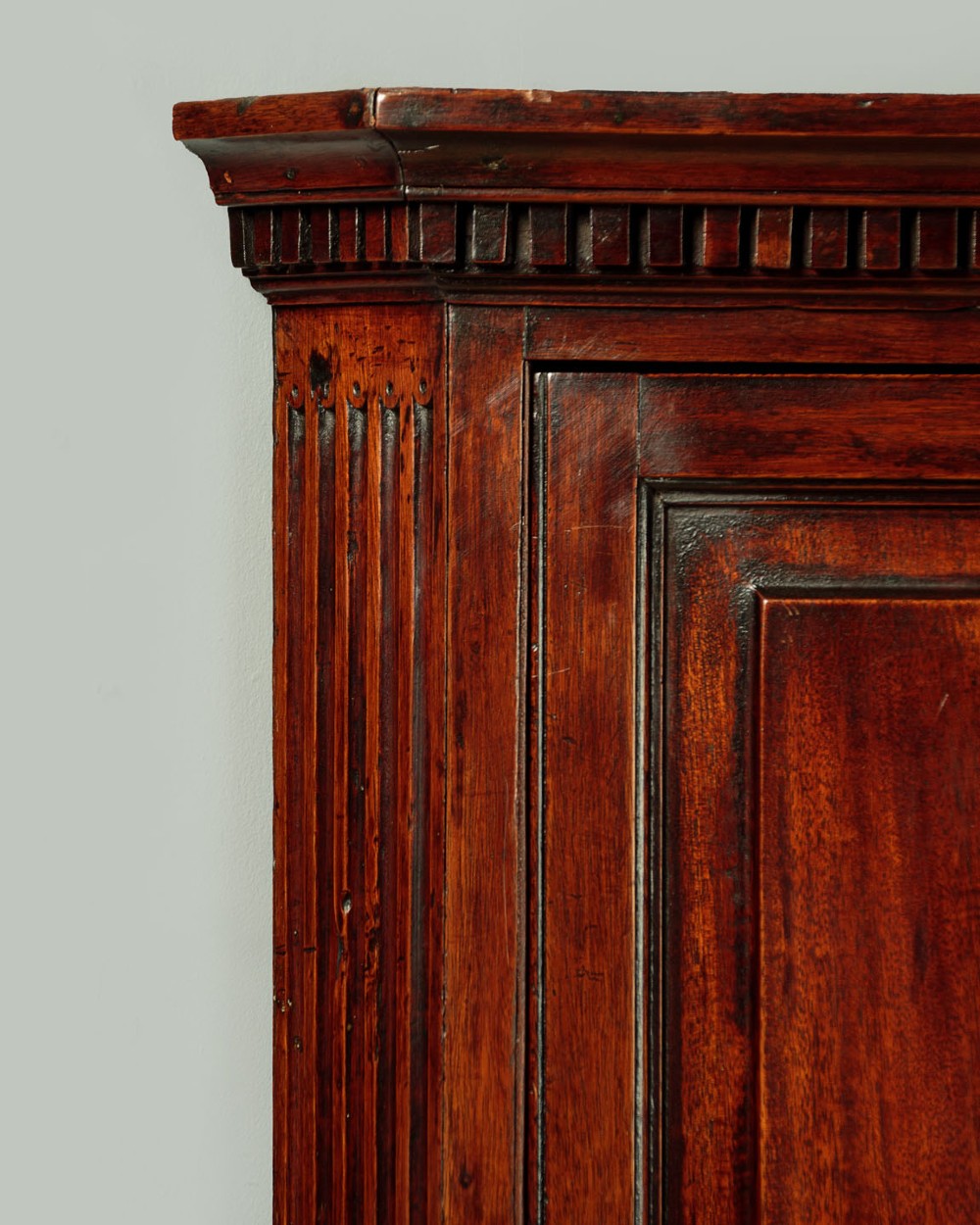 A wall-mounted Georgian mahogany corner cupboard featuring fluted pilasters, dentil moulding, and a single panelled door. View IV