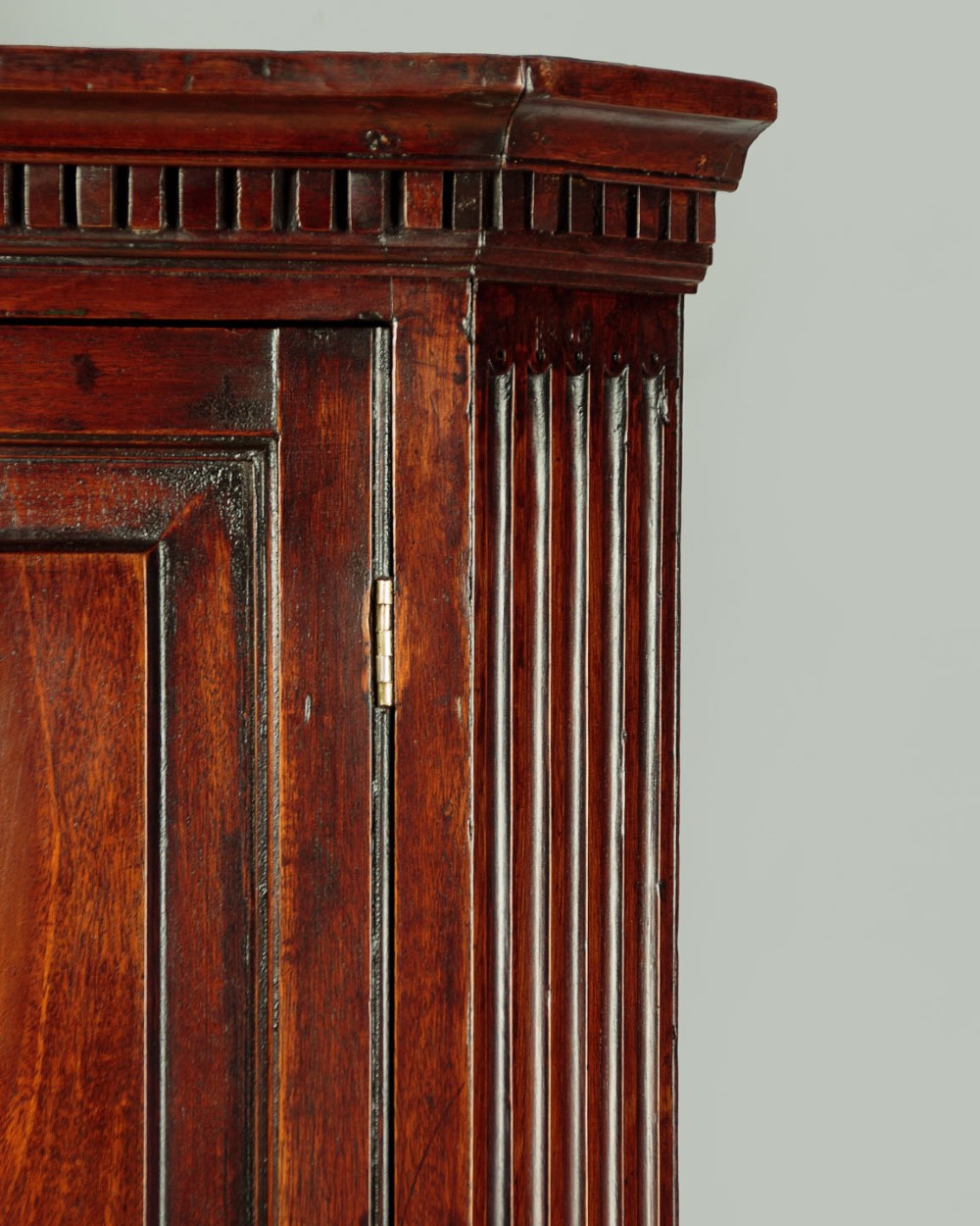 A wall-mounted Georgian mahogany corner cupboard featuring fluted pilasters, dentil moulding, and a single panelled door. View V