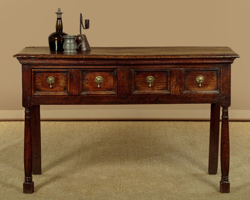 An 18th-century dark oak dresser base featuring geometric moulded drawer fronts, brass drop handles, and turned front legs. View II