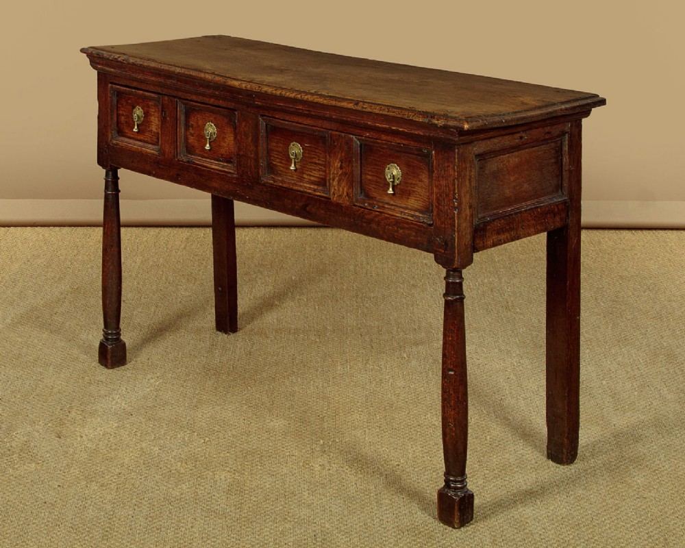 An 18th-century dark oak dresser base featuring geometric moulded drawer fronts, brass drop handles, and turned front legs. View III