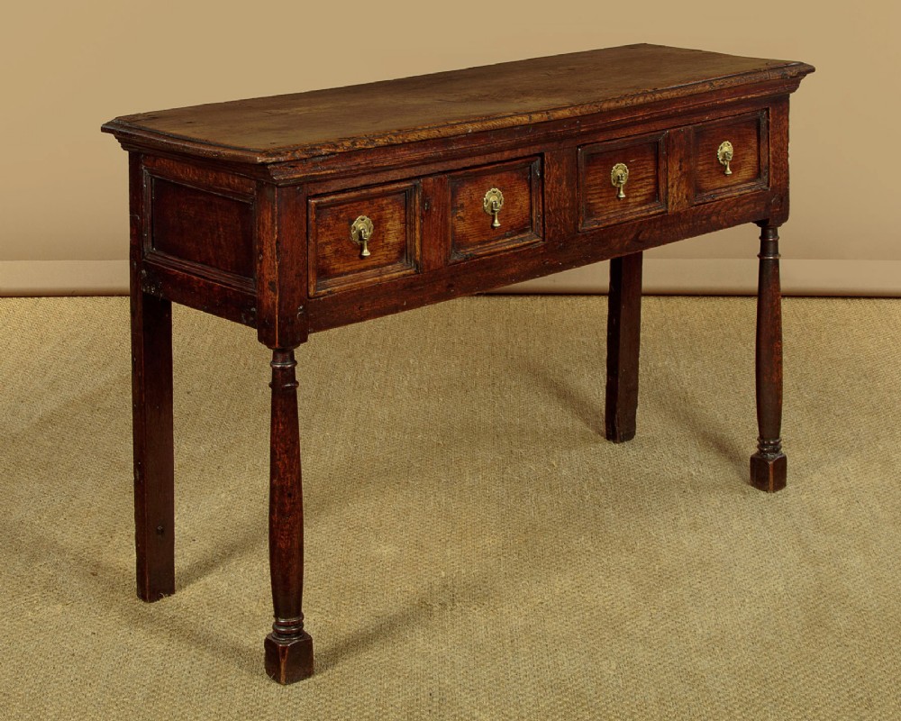 An 18th-century dark oak dresser base featuring geometric moulded drawer fronts, brass drop handles, and turned front legs. View IV