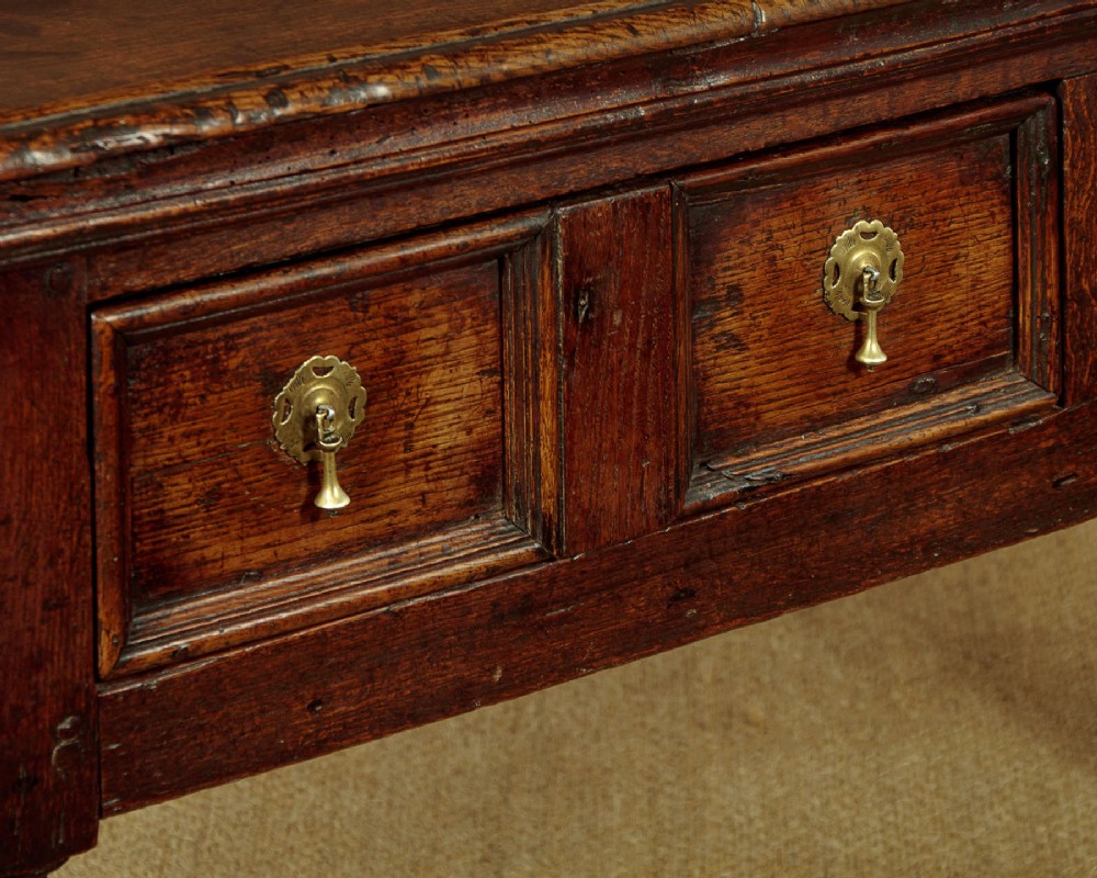 An 18th-century dark oak dresser base featuring geometric moulded drawer fronts, brass drop handles, and turned front legs. View VIII