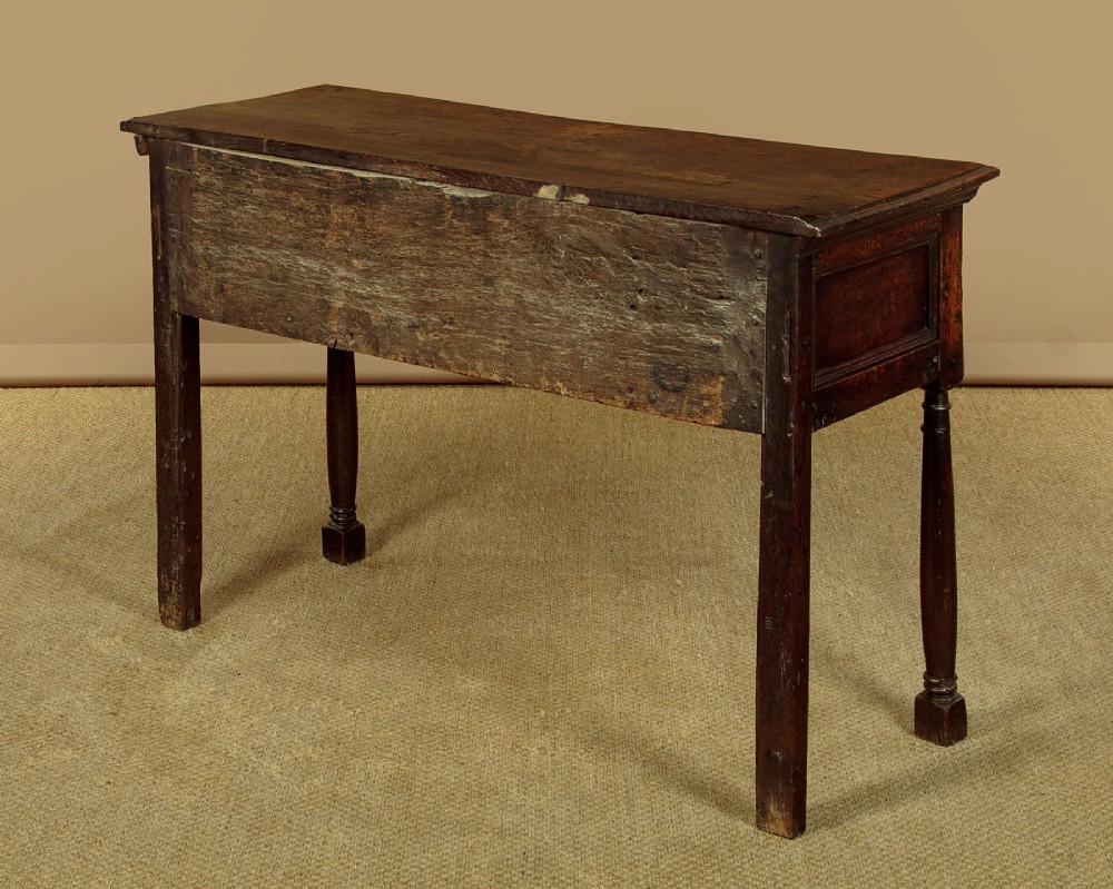 An 18th-century dark oak dresser base featuring geometric moulded drawer fronts, brass drop handles, and turned front legs. View XI