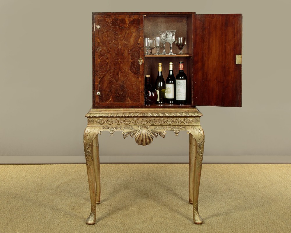 A small veneered brown wood cabinet featuring decorative door pulls, mounted atop a carved silver gilt stand with cabriole legs and a central shell motif. View II