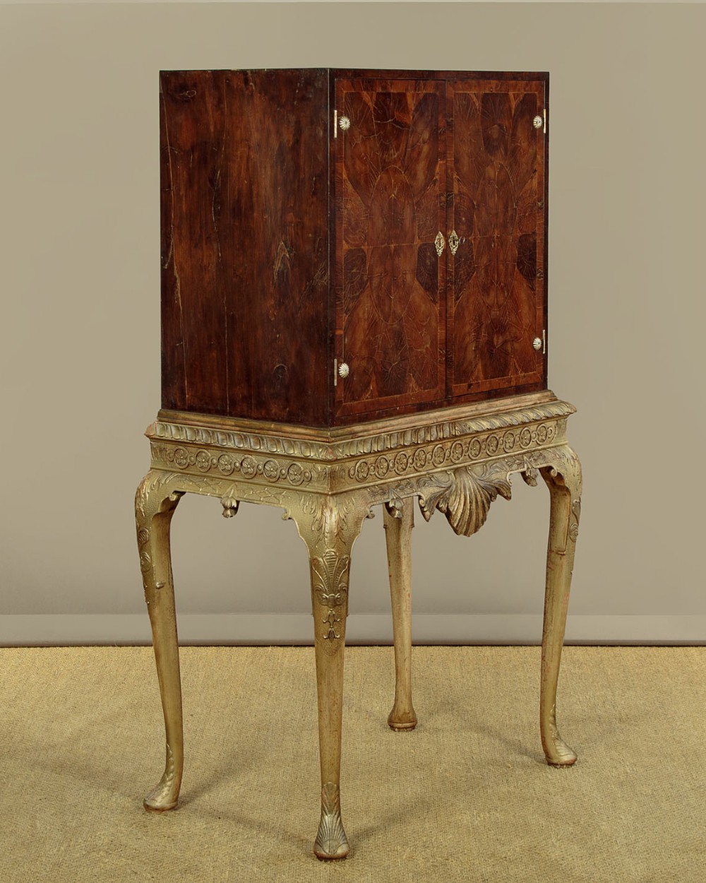 A small veneered brown wood cabinet featuring decorative door pulls, mounted atop a carved silver gilt stand with cabriole legs and a central shell motif. View III
