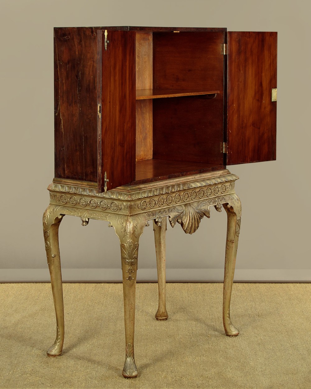 A small veneered brown wood cabinet featuring decorative door pulls, mounted atop a carved silver gilt stand with cabriole legs and a central shell motif. View V