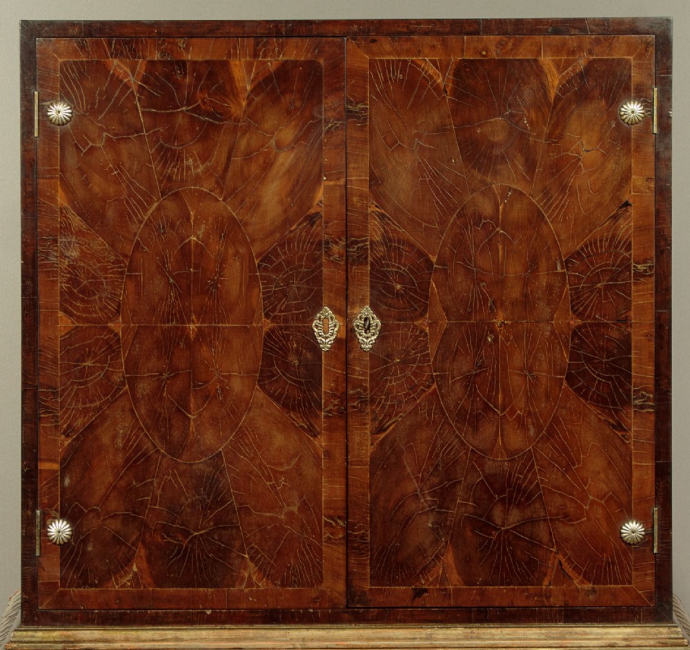 A small veneered brown wood cabinet featuring decorative door pulls, mounted atop a carved silver gilt stand with cabriole legs and a central shell motif. View VI