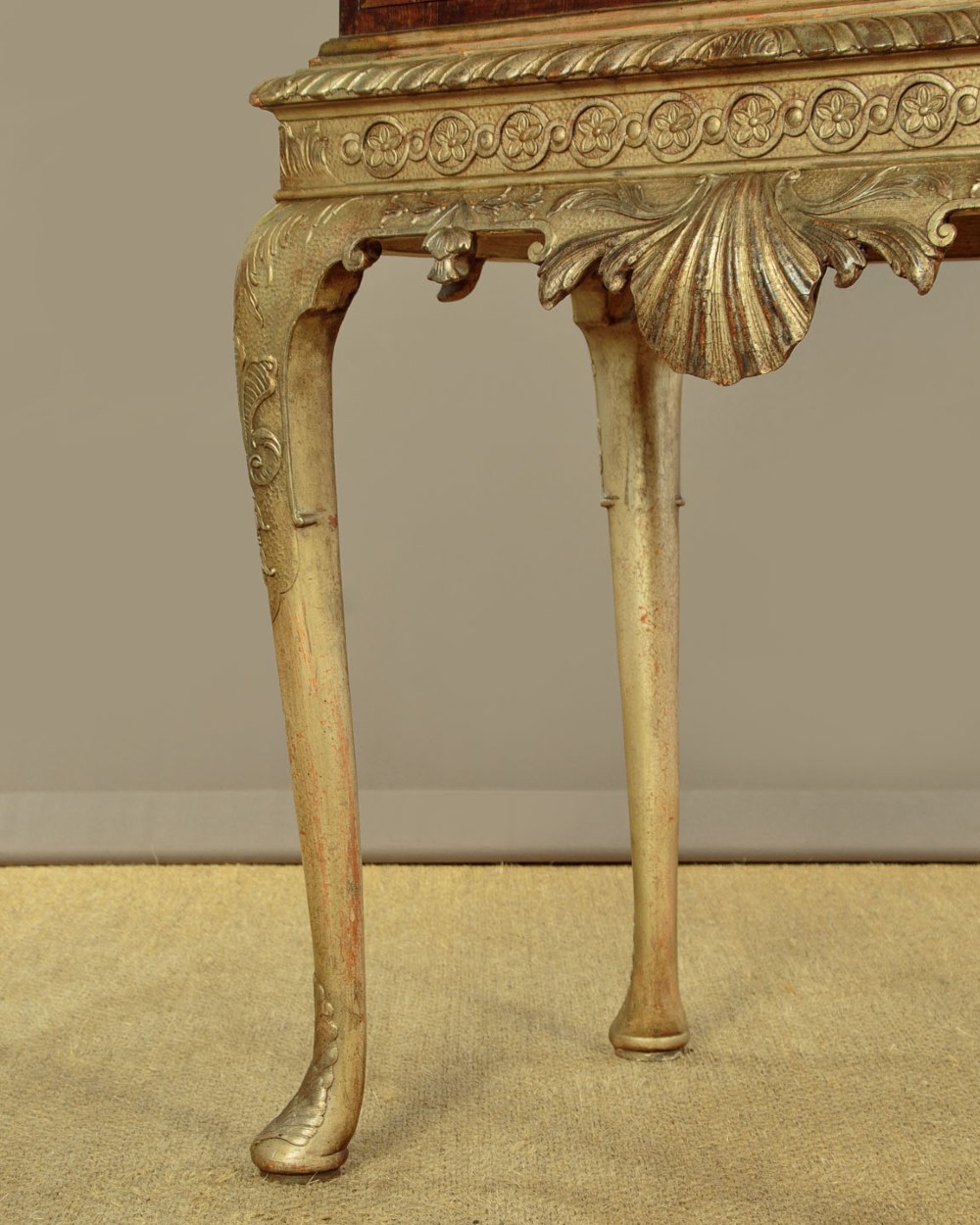 A small veneered brown wood cabinet featuring decorative door pulls, mounted atop a carved silver gilt stand with cabriole legs and a central shell motif. View XII