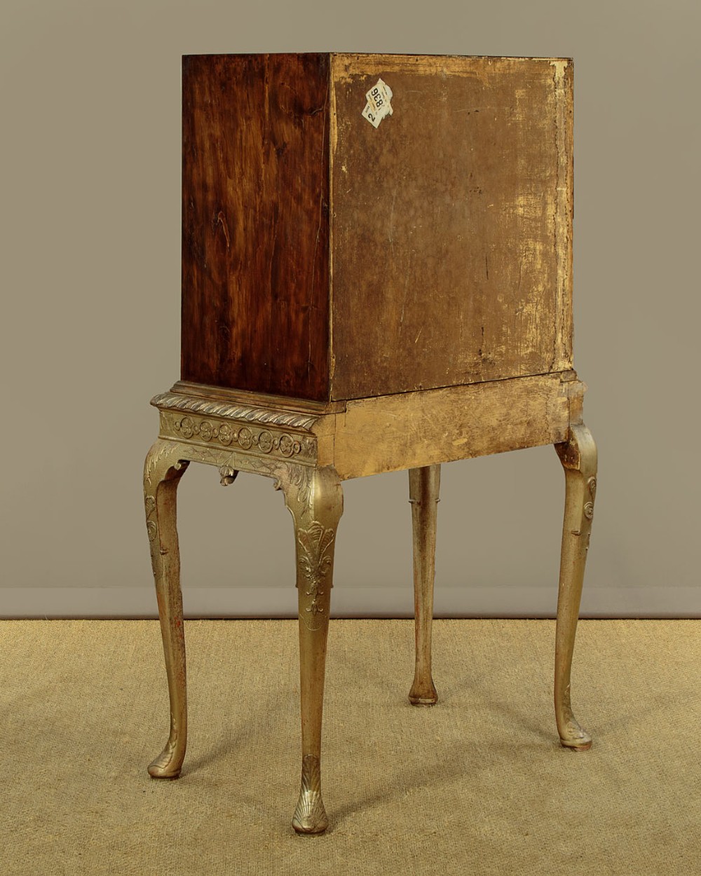 A small veneered brown wood cabinet featuring decorative door pulls, mounted atop a carved silver gilt stand with cabriole legs and a central shell motif. View XIV