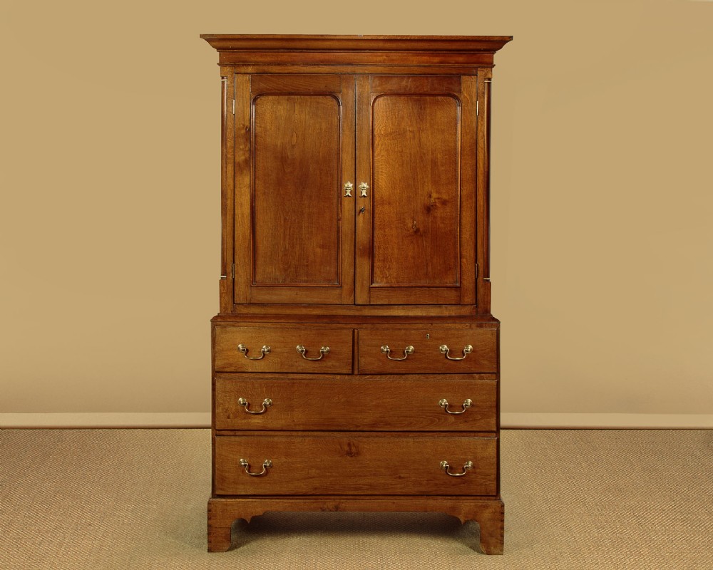 A Georgian Welsh oak press cupboard featuring a two-door upper section with fielded panels above a chest with five drawers and brass handles.
