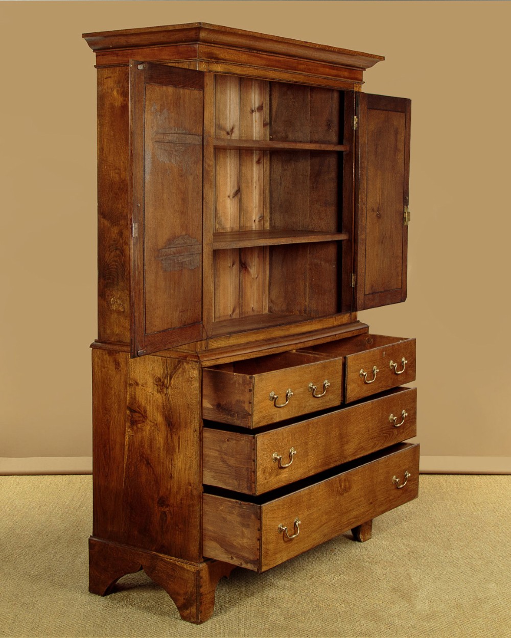 A Georgian Welsh oak press cupboard featuring a two-door upper section with fielded panels above a chest with five drawers and brass handles. View V