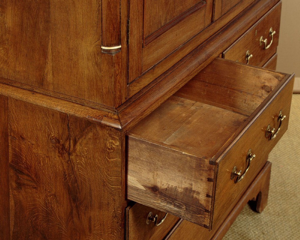 A Georgian Welsh oak press cupboard featuring a two-door upper section with fielded panels above a chest with five drawers and brass handles. View IX