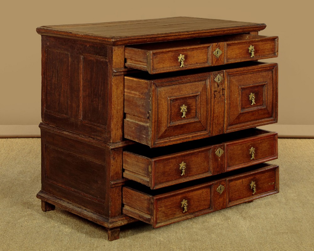 A Charles II solid oak chest of drawers featuring geometric panelled drawer fronts and brass teardrop handles. View IV