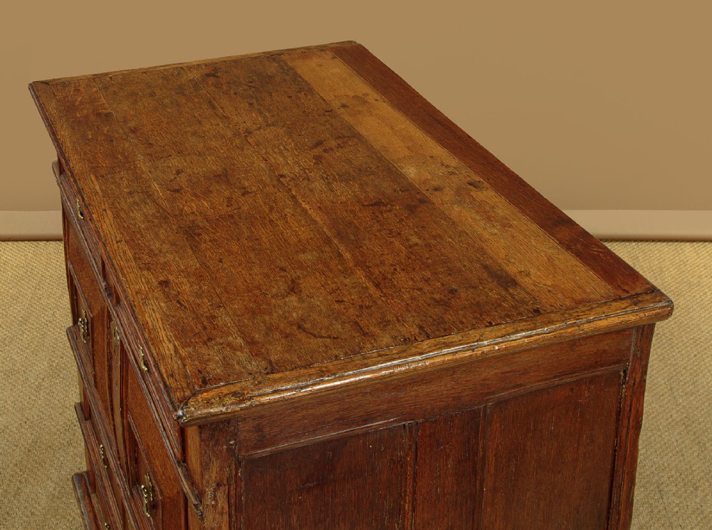 A Charles II solid oak chest of drawers featuring geometric panelled drawer fronts and brass teardrop handles. View V