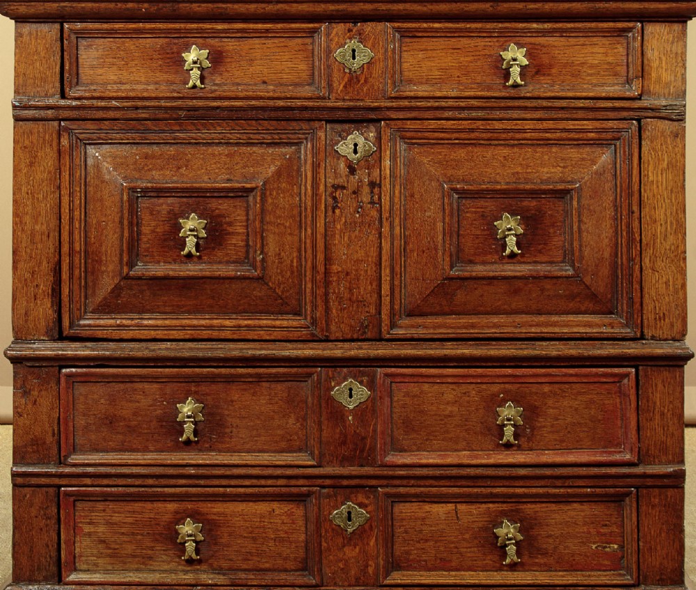 A Charles II solid oak chest of drawers featuring geometric panelled drawer fronts and brass teardrop handles. View VI